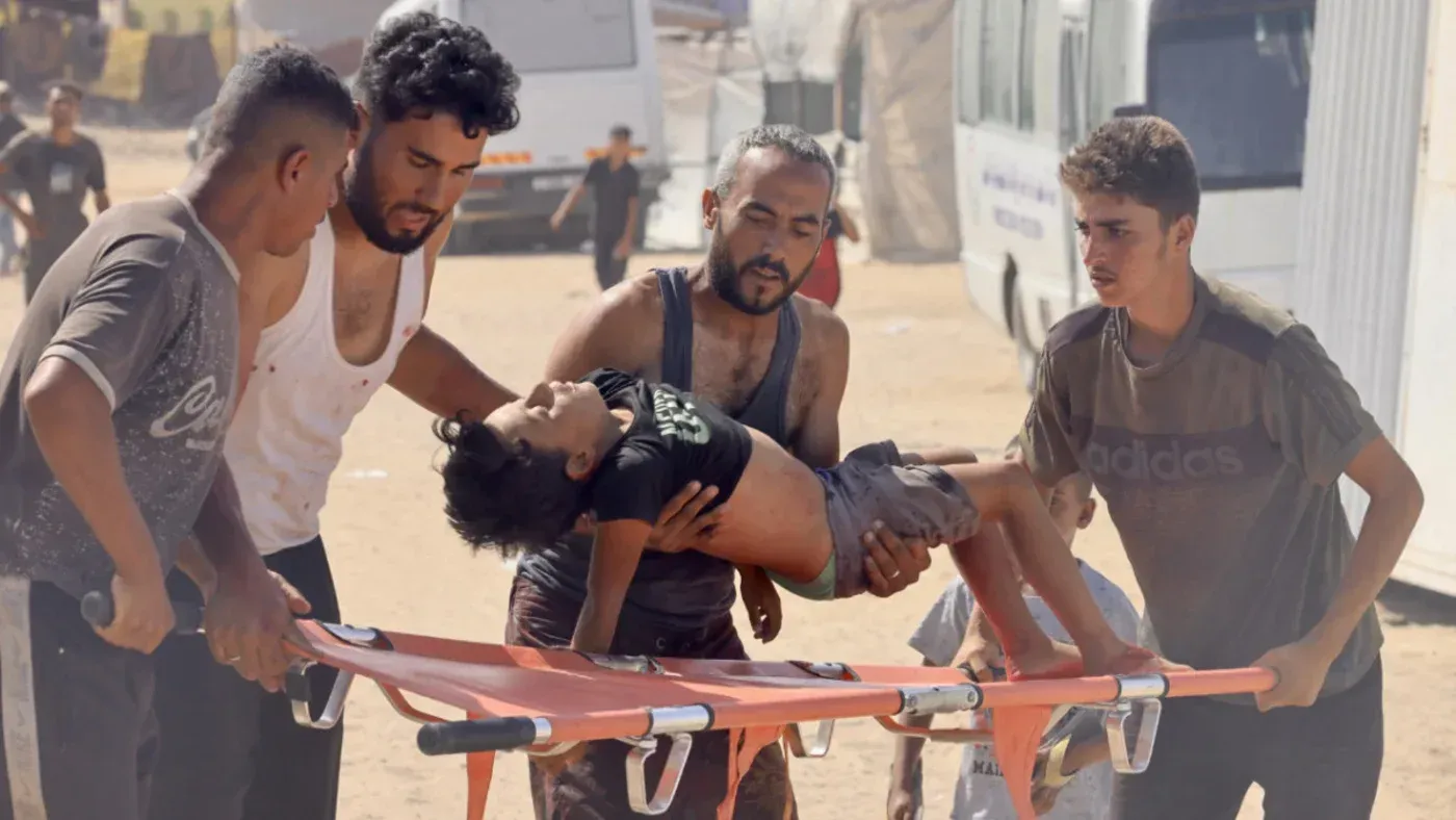 أفراد يحملون طفلاً مصابًا على نقالة في غزة، وسط أجواء من الفوضى، مما يعكس الوضع الإنساني الصعب في المنطقة.