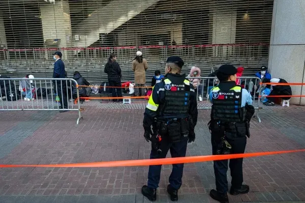 شرطة هونغ كونغ تراقب مجموعة من الأشخاص الجالسين خلف حواجز، في سياق التوترات المتعلقة بقضايا الأمن القومي.