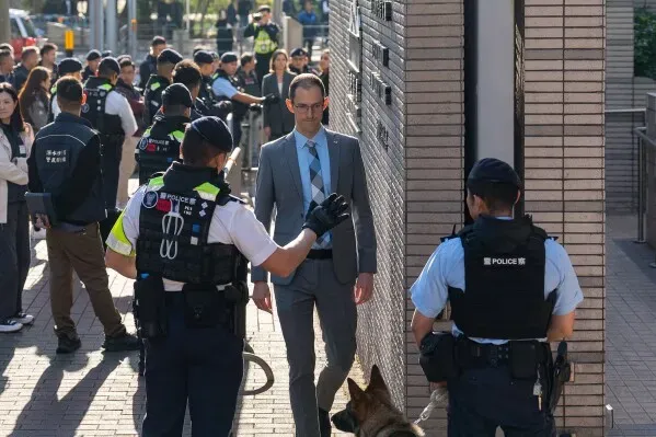 مشهد من محكمة في هونغ كونغ حيث يتواجد رجال شرطة مع كلب بوليسي، بينما يمر رجل يرتدي بدلة رسمية وسط حشد من الناس.