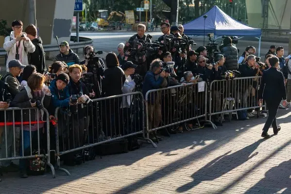 مجموعة من الصحفيين والمصورين يقفون خلف حواجز أثناء تغطيتهم لمحاكمة جيمي لاي في هونغ كونغ، حيث تركزت الأنظار على قضيته المتعلقة بالأمن القومي.