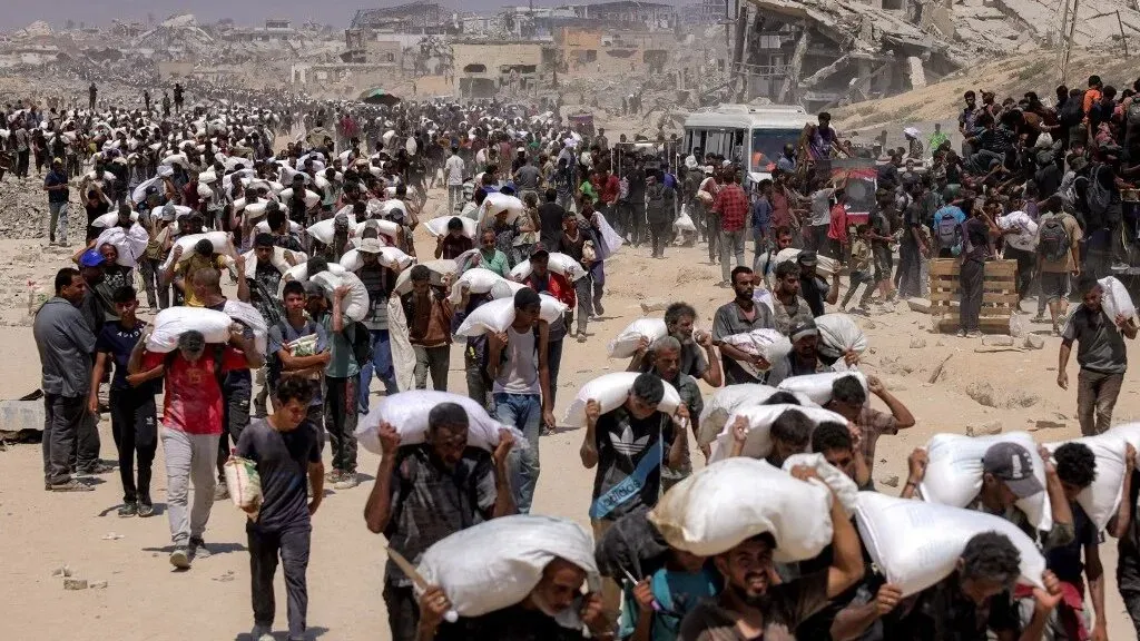 مئات من الفلسطينيين يحملون أكياس المساعدات الغذائية في منطقة مدمرة بغزة، في ظل أزمة إنسانية متزايدة بسبب الحصار.