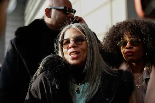 امرأة ترتدي نظارات شمسية وتبتسم، تقف مع شخصين آخرين خارج المحكمة بعد صدور حكم ضد ضابط شرطة سابق في قضية وفاة إريك دوبري.