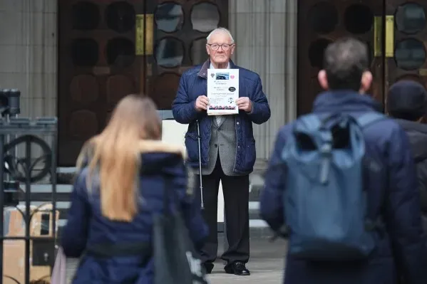 رجل مسن يحمل وثيقة خارج المحكمة العليا في لندن، حيث تُعقد محاكمة جيري آدامز بتهمة المسؤولية عن تفجيرات الجيش الجمهوري الأيرلندي.