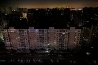 مبنى سكني في كييف مضاء جزئيًا في الليل، مع ظهور بعض النوافذ المضيئة وسط ظلام المدينة بسبب انقطاع الكهرباء المستمر.