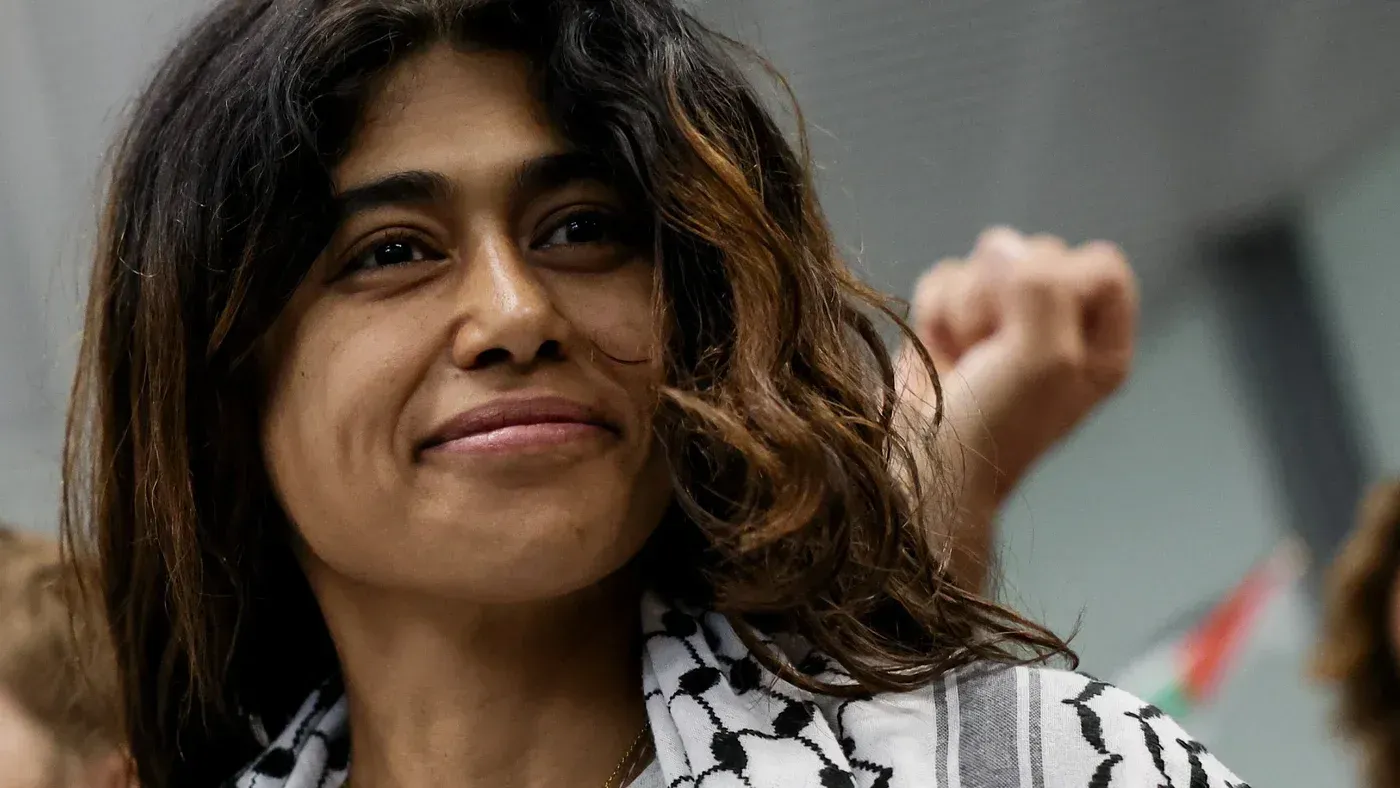 ريما حسن، النائبة الفرنسية الفلسطينية الأصل، مبتسمة وتظهر في خلفية تجمع سياسي، تعكس دعمها للقضية الفلسطينية وسط جدل حول اعتقالها.