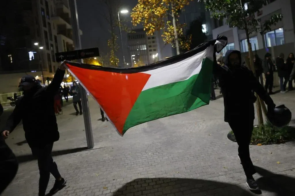 رجل يحمل العلم الفلسطيني في مظاهرة ليلية، تعبيرًا عن الاحتجاج على حظر رفع العلم في شالون-سور-ساون بفرنسا.