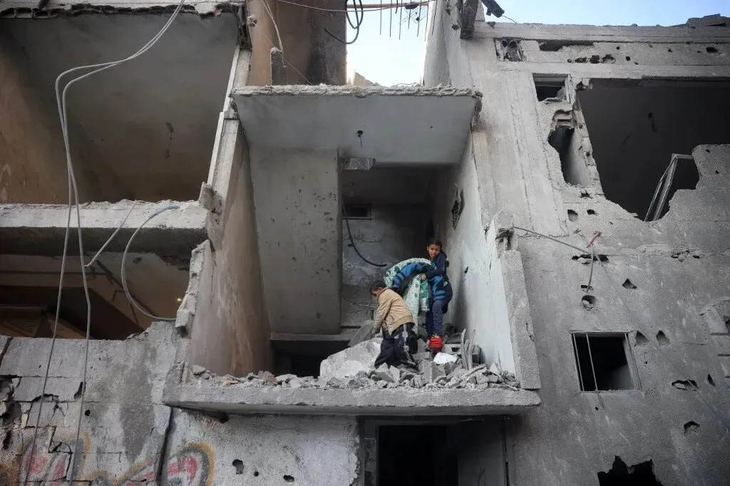 أطفال يتجولون بين أنقاض مبنى مدمر في غزة، حيث يعكس المشهد آثار القصف، وسط أجواء من الدمار والمعاناة الإنسانية.