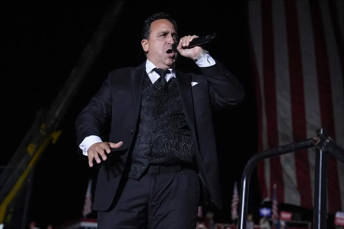 كريستوفر ماتشيو يغني في حفل تنصيب رئيس الولايات المتحدة، محاطًا بعلم أمريكي كبير، ويعكس أجواء الاحتفالات الوطنية.