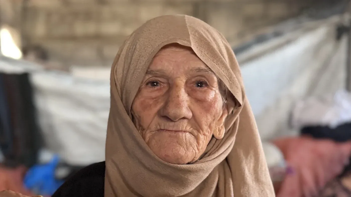وجه امرأة مسنّة ترتدي حجابًا، تعبر عن معاناتها في غزة بعد فقدان عائلتها وبيتها، وسط ظروف قاسية من النزوح والتهجير.