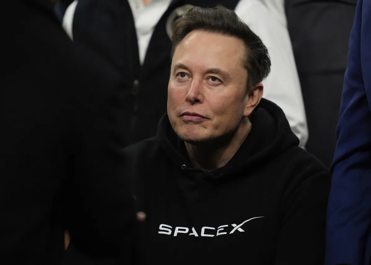إيلون ماسك، مؤسس SpaceX، يظهر في صورة أثناء حدث عام، مرتديًا سترة سوداء تحمل شعار الشركة، مع تعبير جاد يعكس انشغاله بمشاريعه.