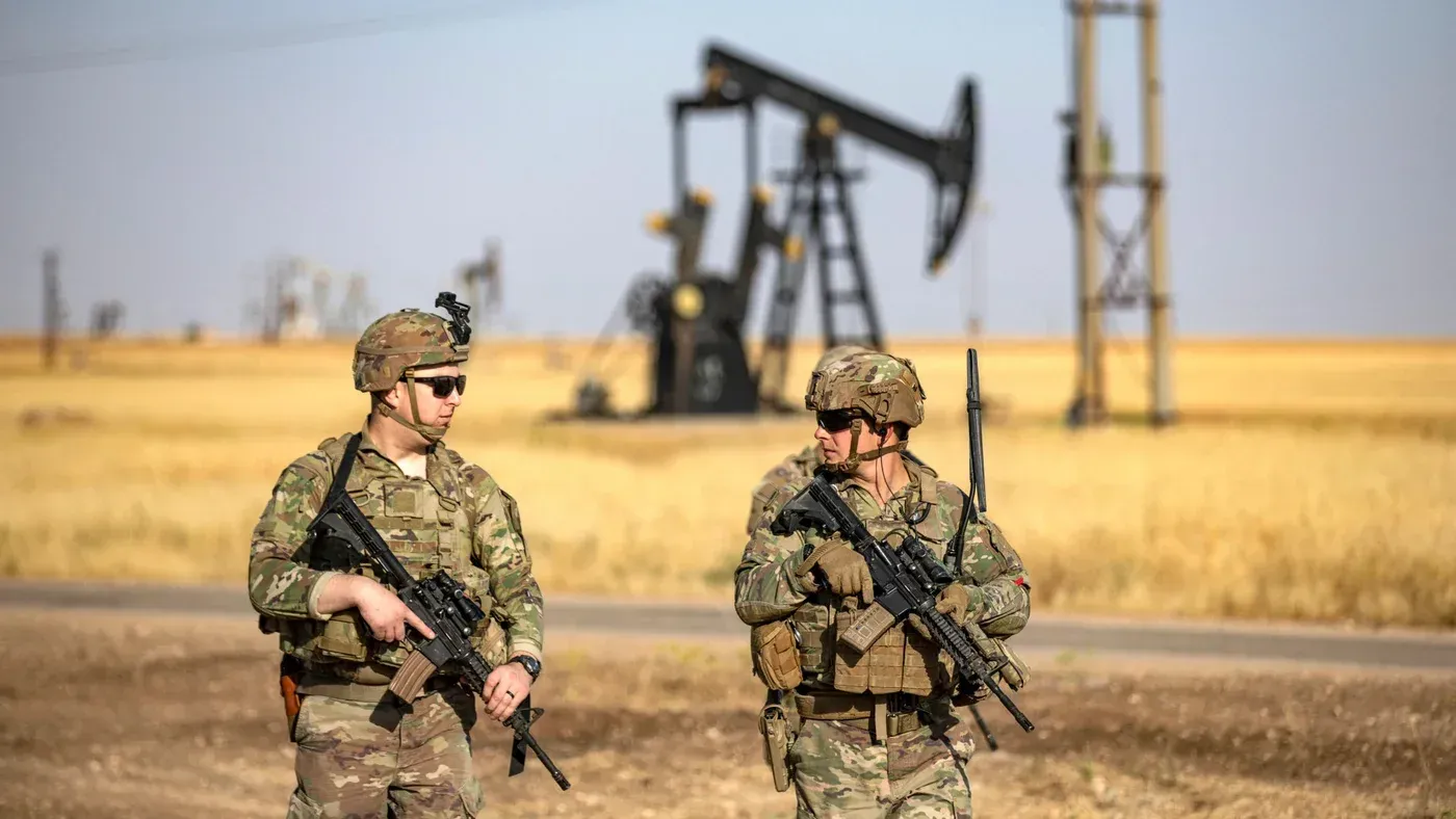 جنود أمريكيون يسيرون بالقرب من منصة نفطية في منطقة صحراوية، مما يعكس التوترات العسكرية حول السيطرة على الموارد النفطية.