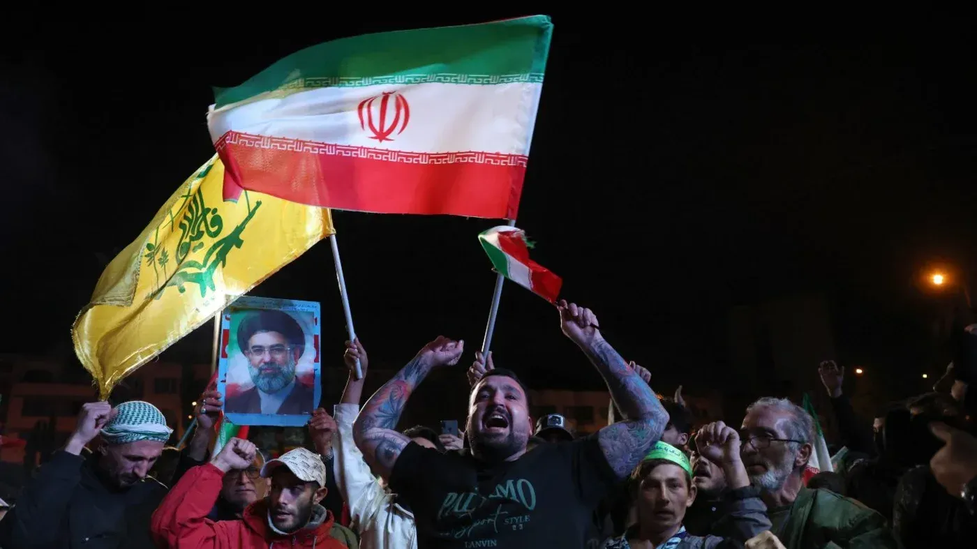 محتجون يحملون علم إيران وعلم حزب الله، مع صورة لقائد إيراني، يعبرون عن دعمهم في سياق التوترات الإقليمية.