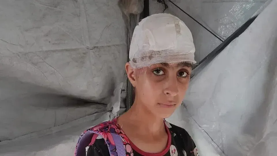 هالة، فتاة تبلغ من العمر 12 عامًا، تظهر برأس مغطى برباط طبي، تعكس معاناتها بعد إصابتها خلال غارة جوية في غزة.