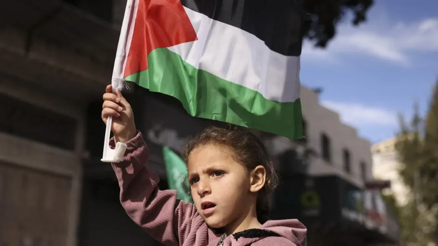 طفلة تحمل علم فلسطين في مظاهرة، تعبر عن دعمها للقضية الفلسطينية وسط أجواء من التوتر في غزة.