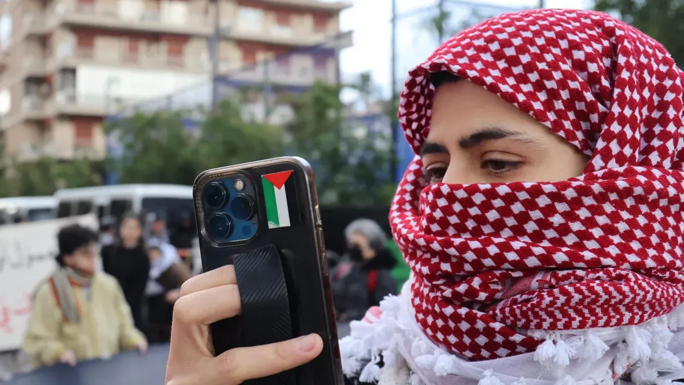 امرأة ترتدي الكوفية الفلسطينية وتستخدم هاتفها المحمول أثناء حركة احتجاجية، تعبيراً عن دعمها للقضية الفلسطينية.
