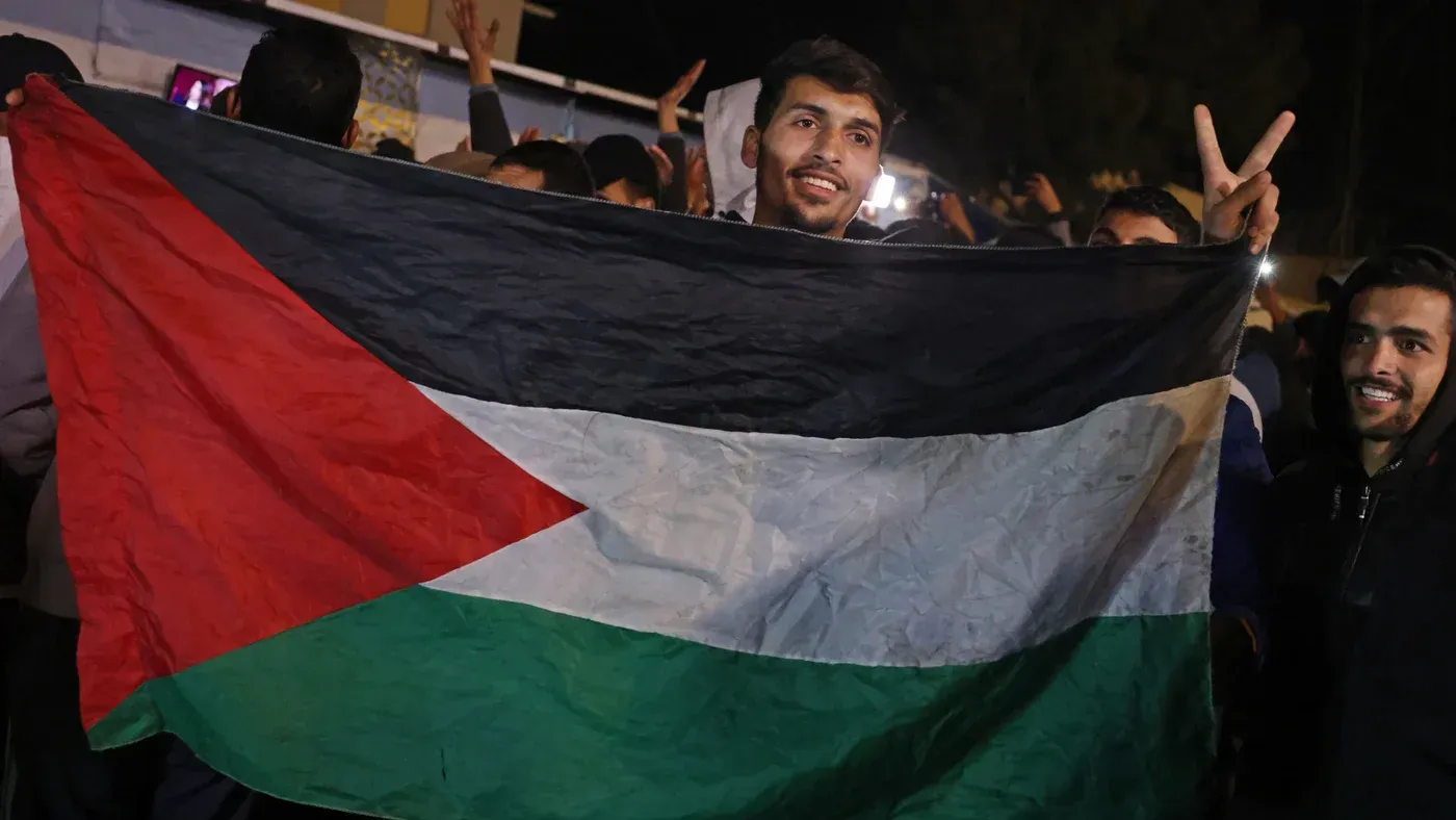 شخص يحمل علم فلسطين في تجمع حاشد، مع تعبير عن الفرح والأمل وسط الأجواء السياسية المتوترة في المنطقة.