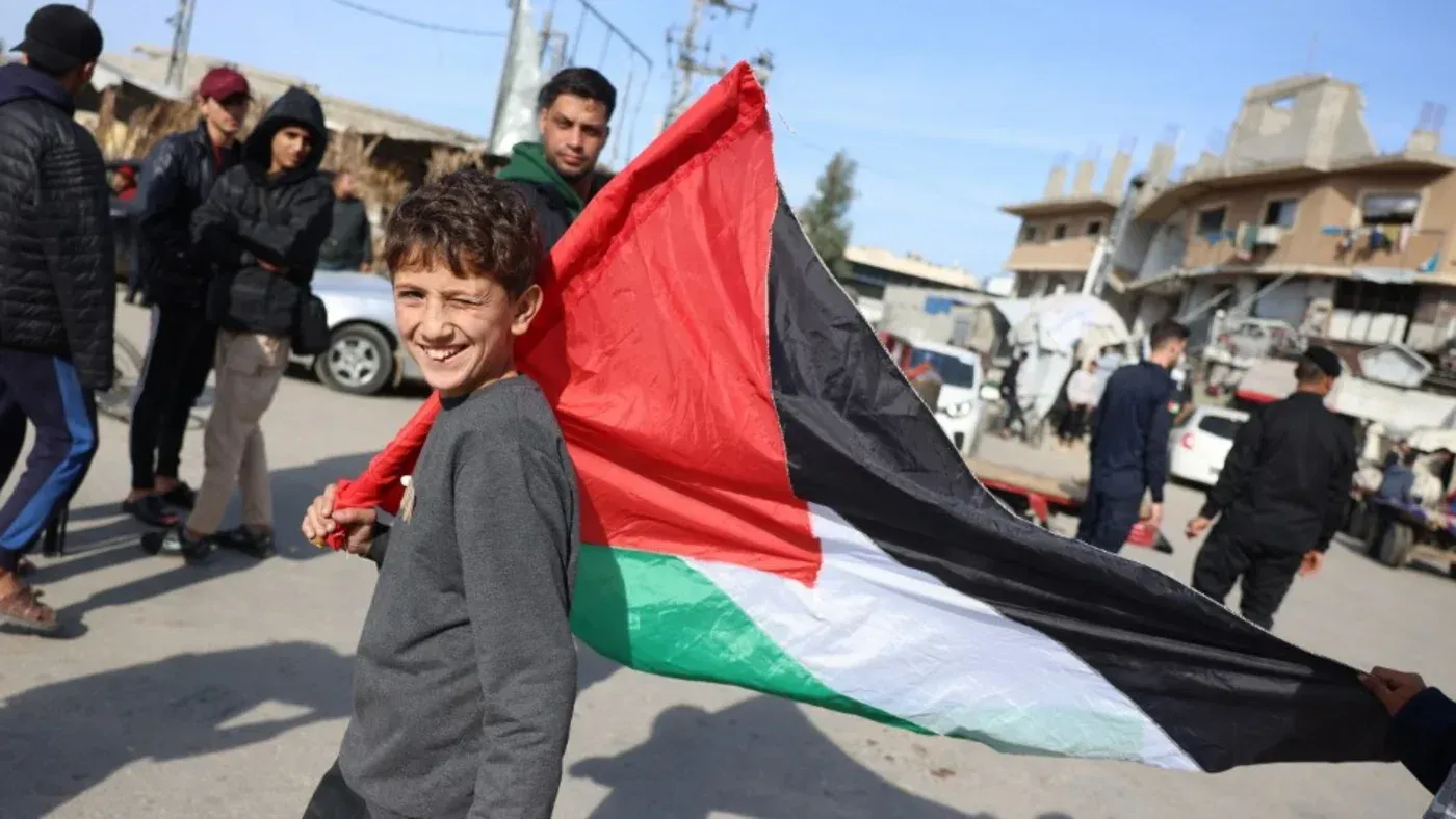 طفل يحمل علم فلسطين في وسط تجمع حاشد في غزة، مع خلفية لأشخاص ومبانٍ مدمرة، يعكس روح المقاومة والأمل في مستقبل أفضل.