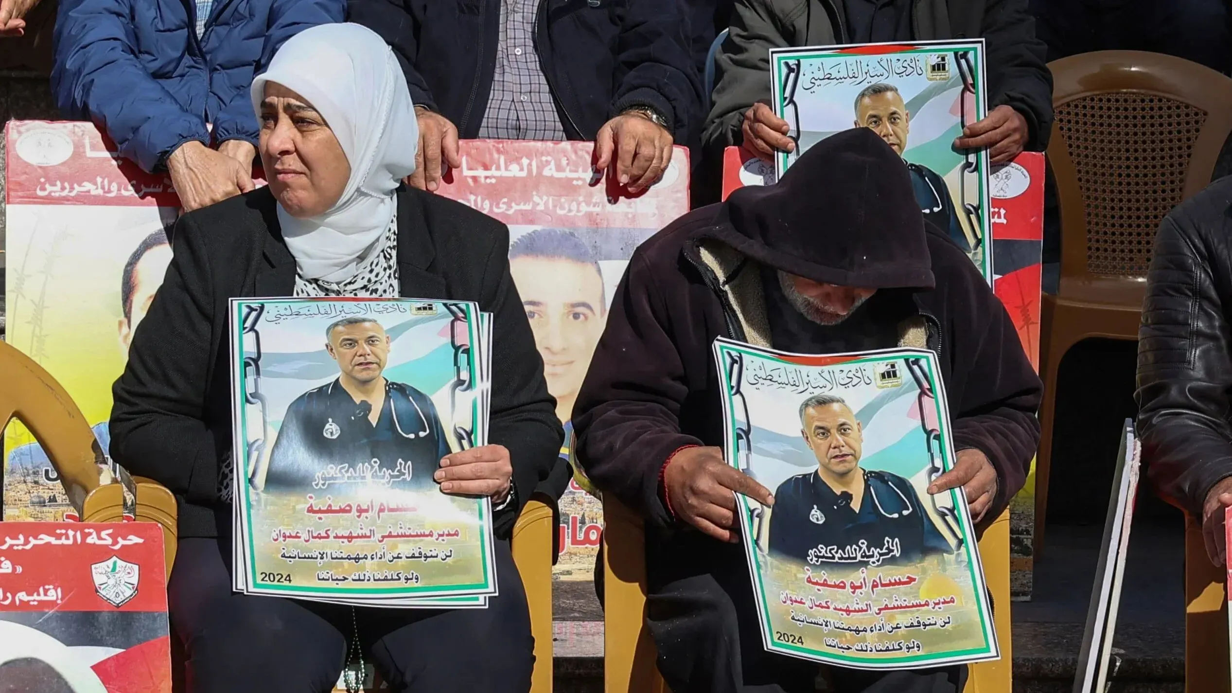 تظهر الصورة عائلة وأصدقاء الدكتور حسام أبو صفية في تجمع احتجاجي، يحملون لافتات تدعو للإفراج عنه، مع التركيز على معاناته في السجون الإسرائيلية.