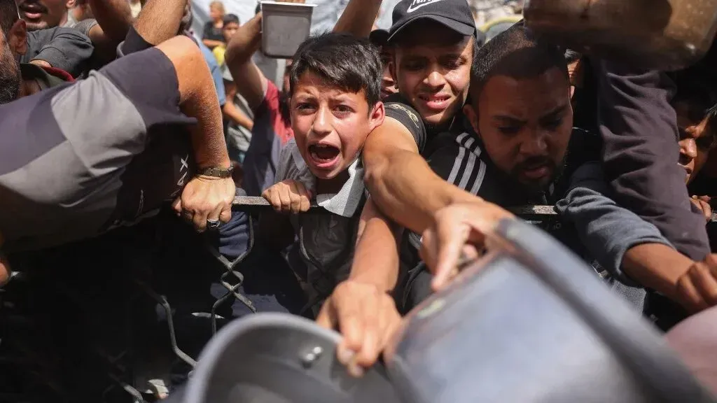 صبي صغير يصرخ وسط حشد من الناس الذين يتزاحمون للحصول على الطعام في غزة، مما يعكس أزمة الجوع المتزايدة.