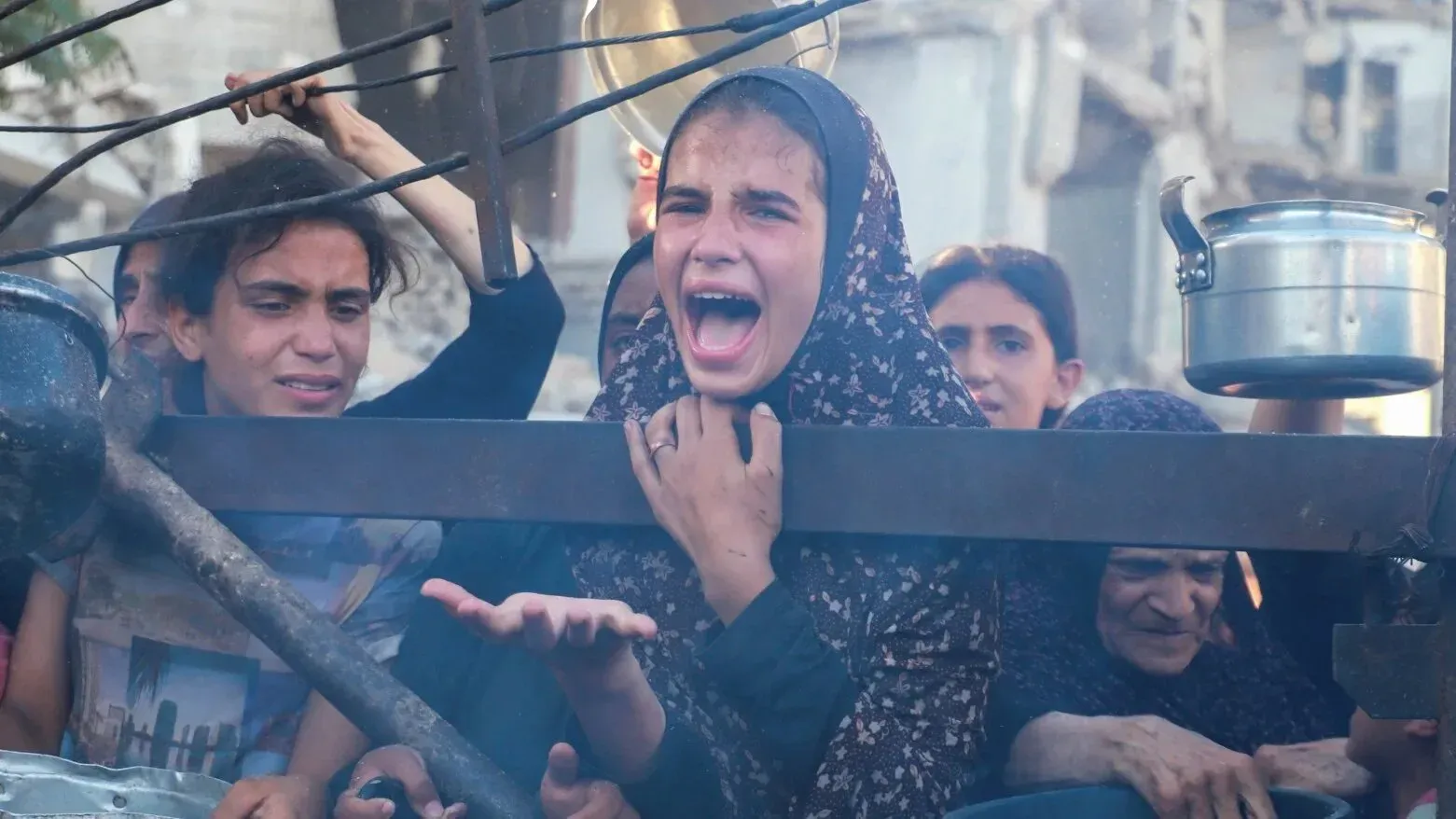 نساء وأطفال يتجمعون في طابور للحصول على الطعام في غزة، مع تعبيرات وجه تعكس الألم والمعاناة بسبب الجوع.