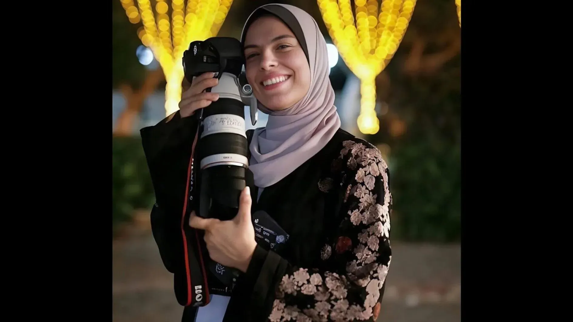 فاطمة حسونة، مصورة صحفية في غزة، تبتسم وتحتضن كاميرتها، تعبيرًا عن شغفها في توثيق الحياة اليومية رغم الظروف الصعبة.