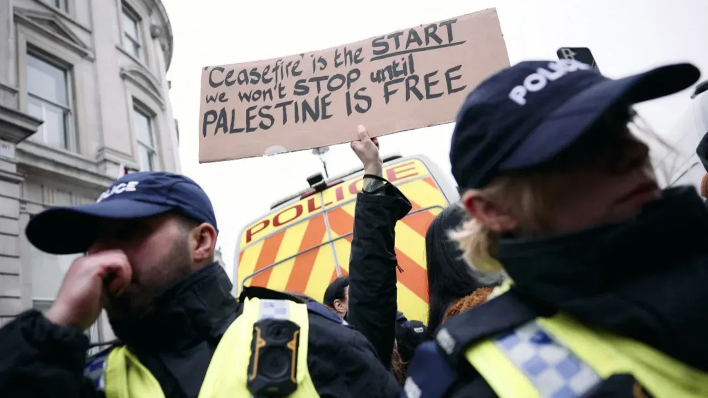 لافتة تحمل شعار "الهدنة هي البداية، لن نتوقف حتى تتحرر فلسطين" مع وجود رجال شرطة في الخلفية خلال مظاهرة في لندن.