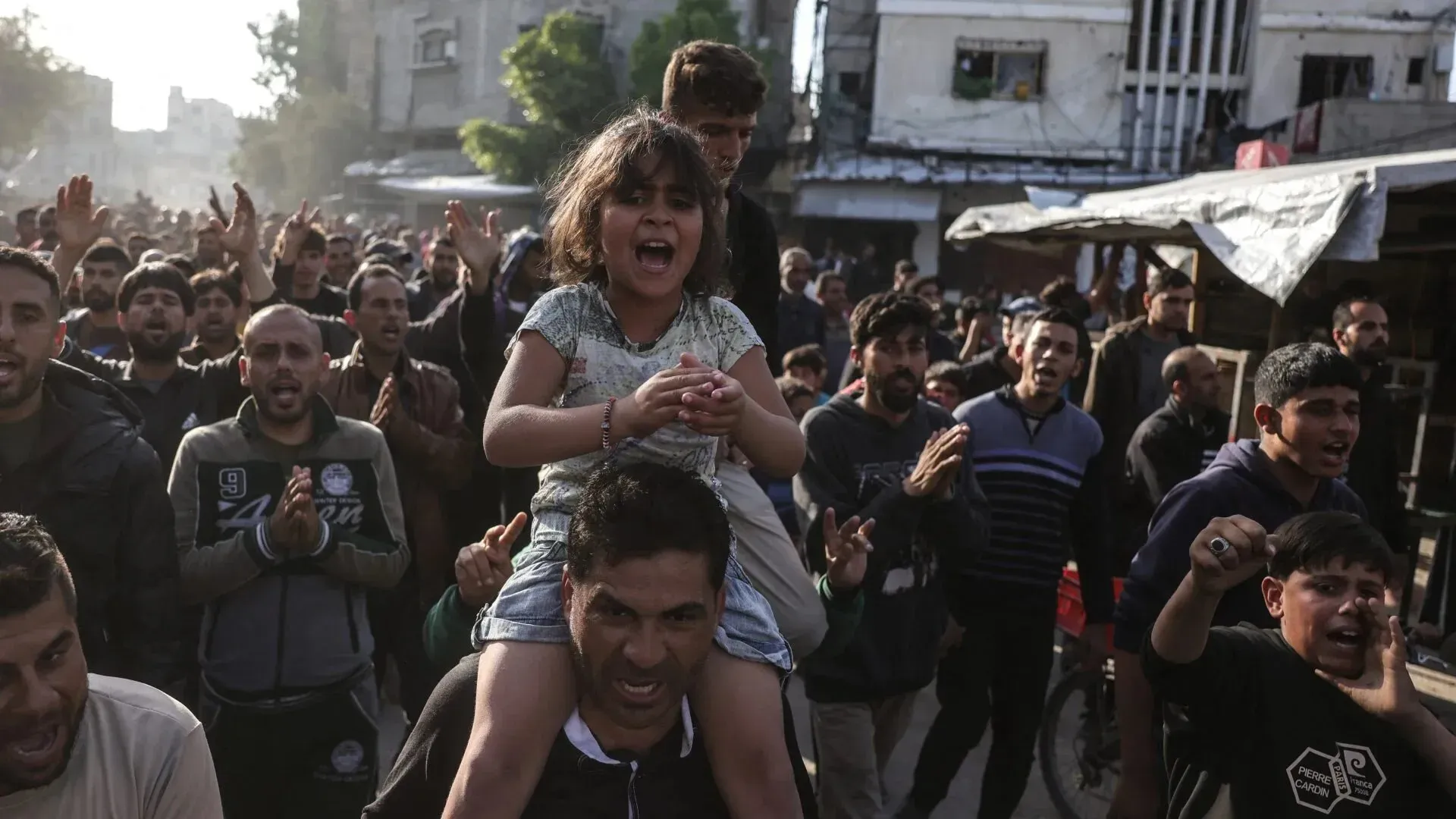 حشود من المتظاهرين في غزة، بينهم فتاة صغيرة على كتف والدها، يعبرون عن غضبهم من الحرب والاحتلال الإسرائيلي.