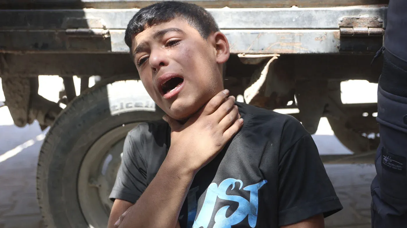طفل فلسطيني يبكي بحرقة، ممسكًا برقبته، في مشهد يعكس معاناة المدنيين خلال التصعيد العسكري في غزة.