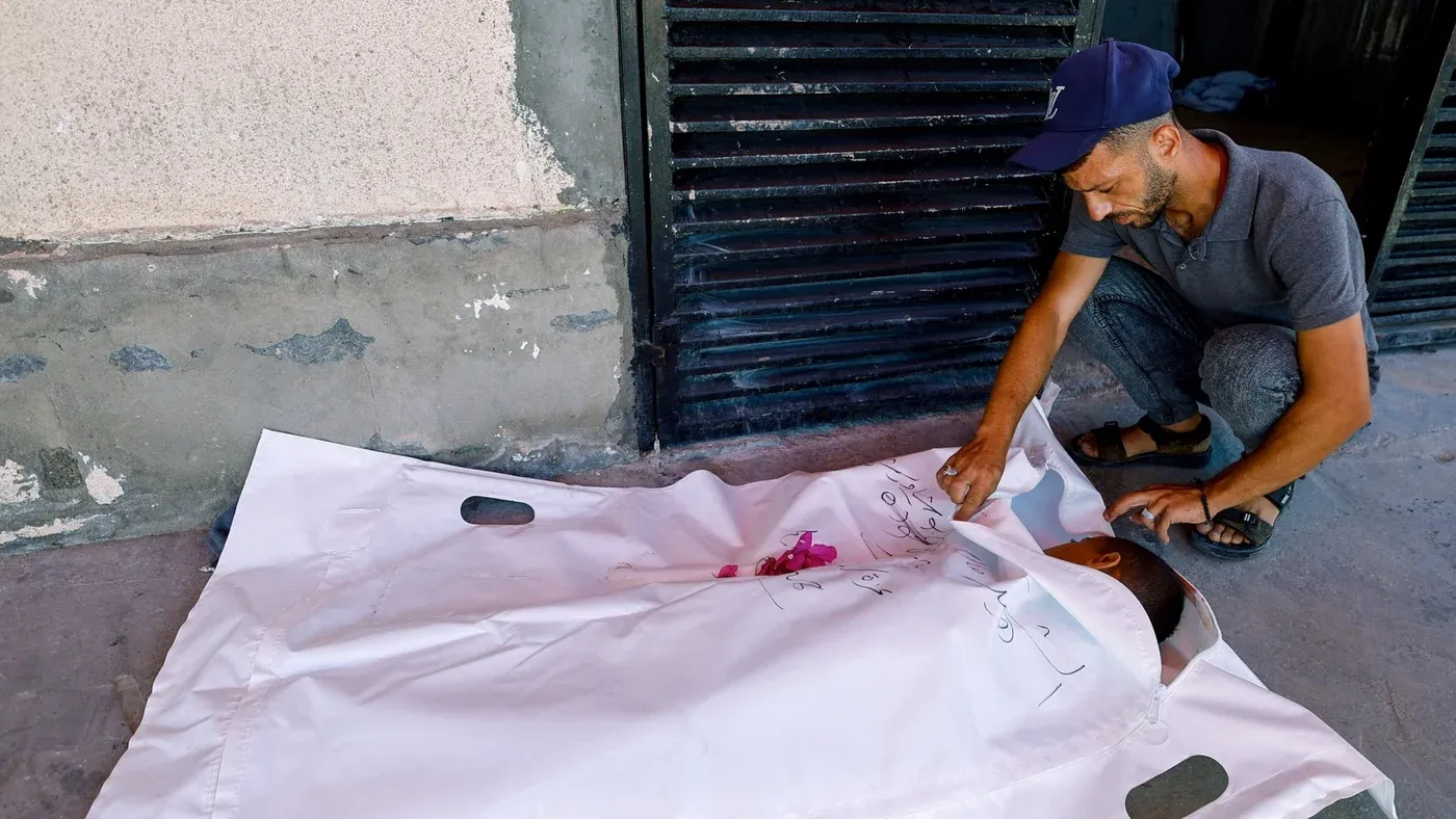 رجل فلسطيني يودع جثمان طفل ملفوف في كيس أبيض وسط الحصار الصحي والإنساني في غزة.