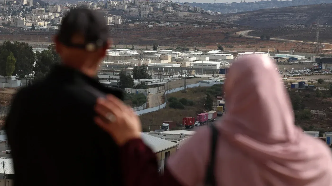 شخصان يقفان متجاورين، ينظران إلى سجن فلسطيني، مما يعكس معاناة الأسرى والاعتقالات الجماعية في الضفة الغربية.