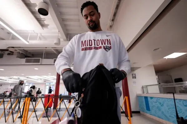 طالب في مدرسة ميدتاون الثانوية يقوم بتفتيش حقيبته عند نقطة فحص الأسلحة، وسط أجواء مدرسية حديثة.