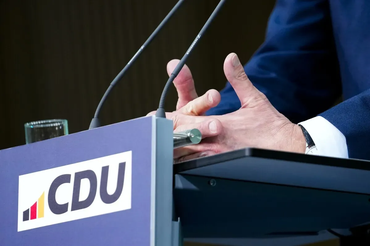 يد تظهران على طاولة مؤتمر صحفي مع شعار حزب CDU، تعبر عن أهمية اتخاذ إجراءات عاجلة لمعالجة الركود الاقتصادي في ألمانيا.