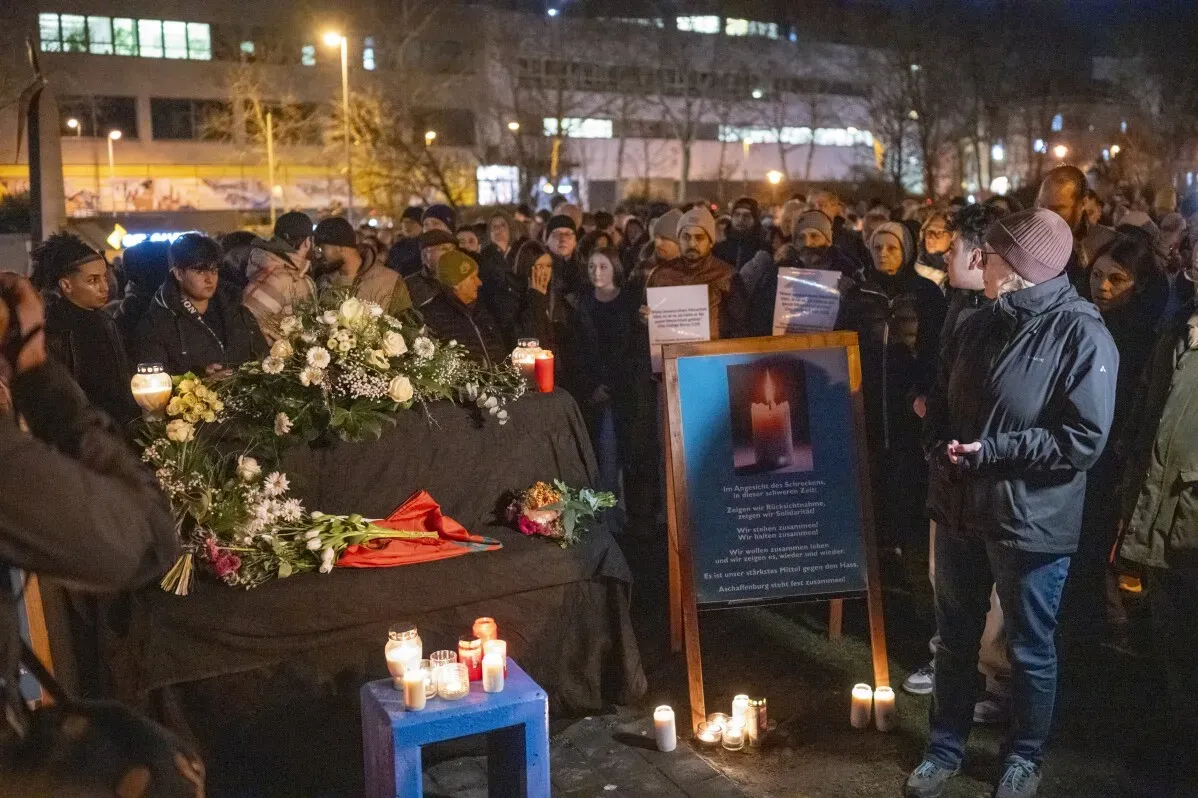 تجمع حشد من الأشخاص حول منصة تذكارية في ألمانيا، تحتوي على زهور وشموع، لتكريم ضحايا الهجوم بسكين.