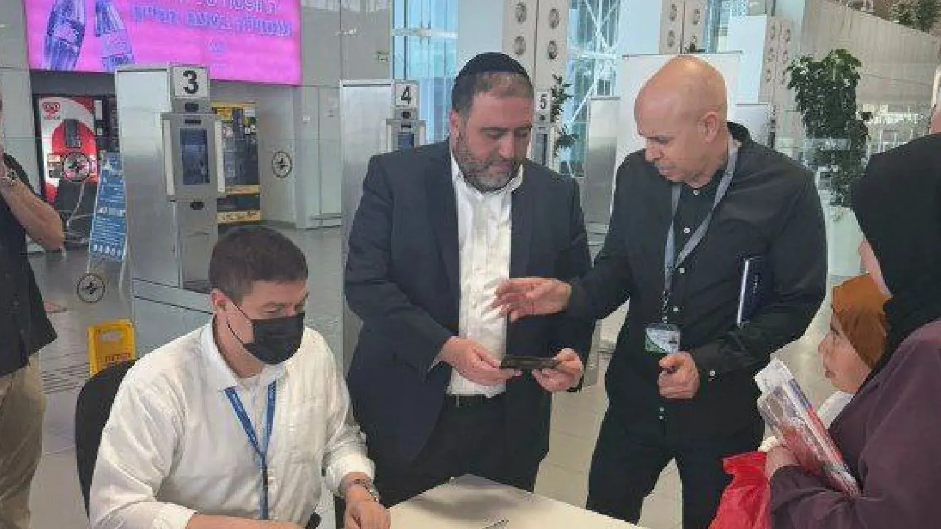 اجتماع مسؤولين إسرائيليين في مطار رامون لمناقشة مغادرة الفلسطينيين من غزة، مع امرأة ترتدي حجابًا في الخلفية.