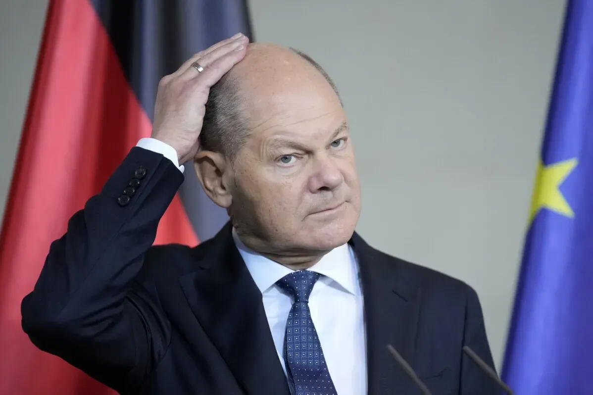 المستشار الألماني أولاف شولتز يتحدث بجدية خلال مؤتمر صحفي، مع العلم الألماني وخلفية علم الاتحاد الأوروبي، معبرًا عن انتقاداته لإيلون ماسك.