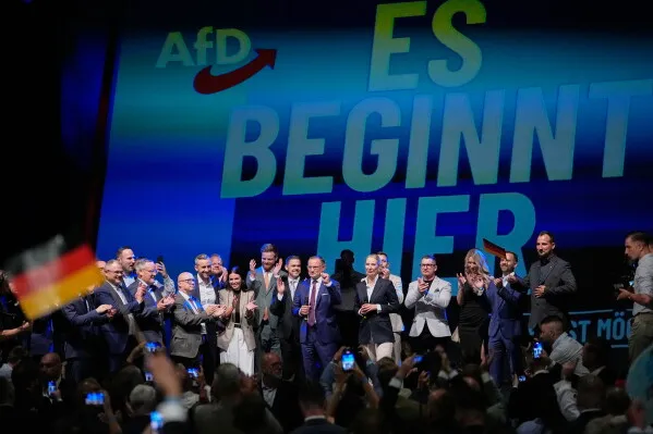 احتفال قادة حزب البديل من أجل ألمانيا AfD بفوزهم الانتخابي في ولاية ساكسونيا-أنهالت وسط حشد مؤيدين، مع شعار الحزب في الخلفية.