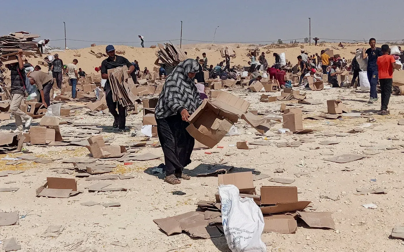 مشهد لعدد من الأشخاص في موقع توزيع المساعدات الإنسانية في غزة، حيث يقومون بجمع صناديق كرتونية وسط ظروف صعبة.