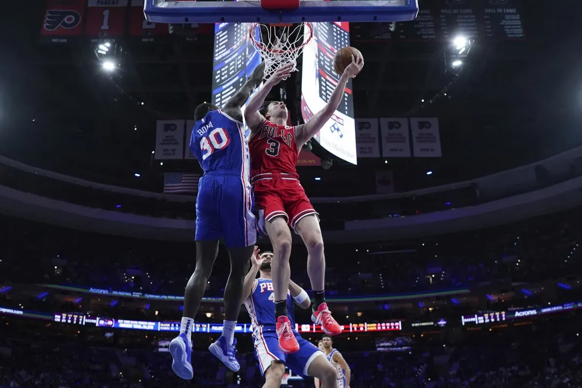 لاعب من فريق شيكاغو بولز يسجل نقطة خلال مباراة ضد فيلادلفيا 76ers، حيث يظهر في الخلفية لاعب من الفريق المنافس.