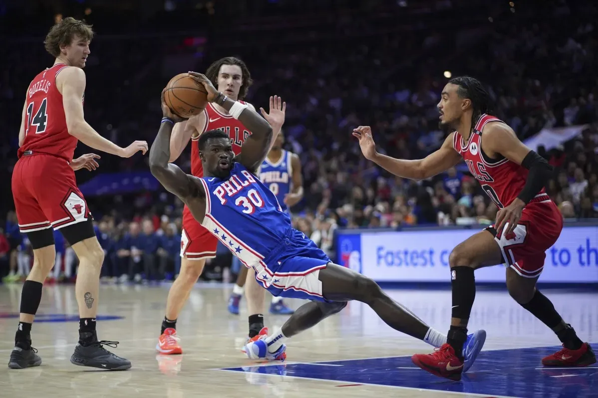 لاعب من فريق فيلادلفيا 76ers يسقط على الأرض محاولاً السيطرة على الكرة، بينما يتنافس معه لاعبان من فريق شيكاغو بولز في مباراة حماسية.