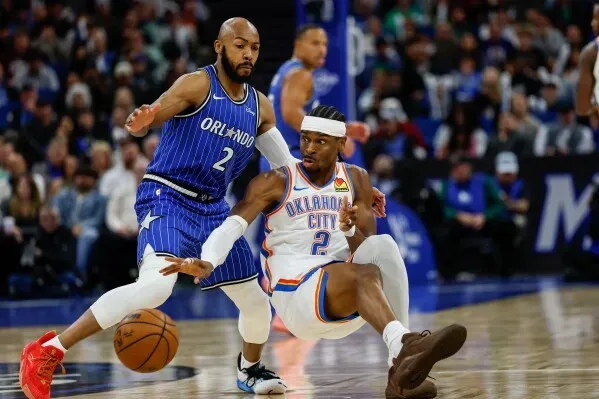 لاعب من فريق أورلاندو ماجيك يتصدى للاعب من فريق أوكلاهوما سيتي ثاندر خلال مباراة كرة سلة، مع وجود لاعبين آخرين في الخلفية.