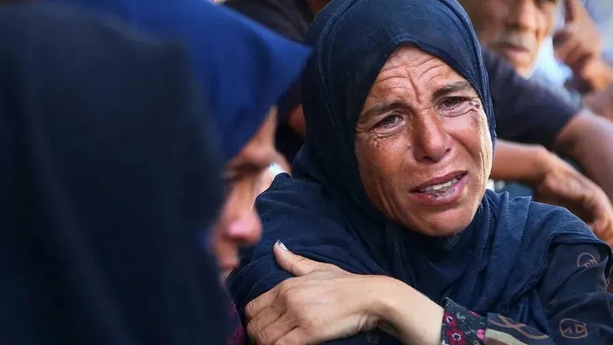 امرأة فلسطينية تبكي في تجمع، تعبر عن الحزن العميق بسبب الأوضاع الإنسانية الصعبة في غزة، وسط مشهد من الألم والمعاناة.