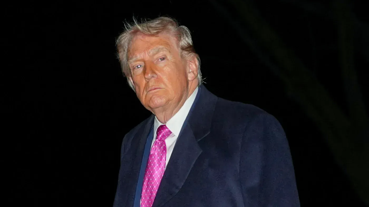 تعبير جاد عن الرئيس الأمريكي السابق دونالد ترامب، يرتدي بدلة داكنة وربطة عنق وردية، يظهر في أجواء مظلمة، مما يعكس التوترات السياسية الحالية.