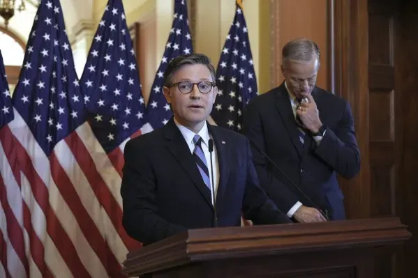 النائب خوان سيسكوماني يتحدث في مؤتمر صحفي، مع أعلام أمريكية خلفه، حول قضايا برنامج Medicaid وتأثيره على الناخبين.
