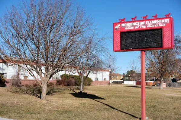 مدرسة مورنينغسايد الابتدائية في غريت فولز، مع لافتة تشير إلى أنها "موطن الخيول"، محاطة بأشجار في يوم مشمس.