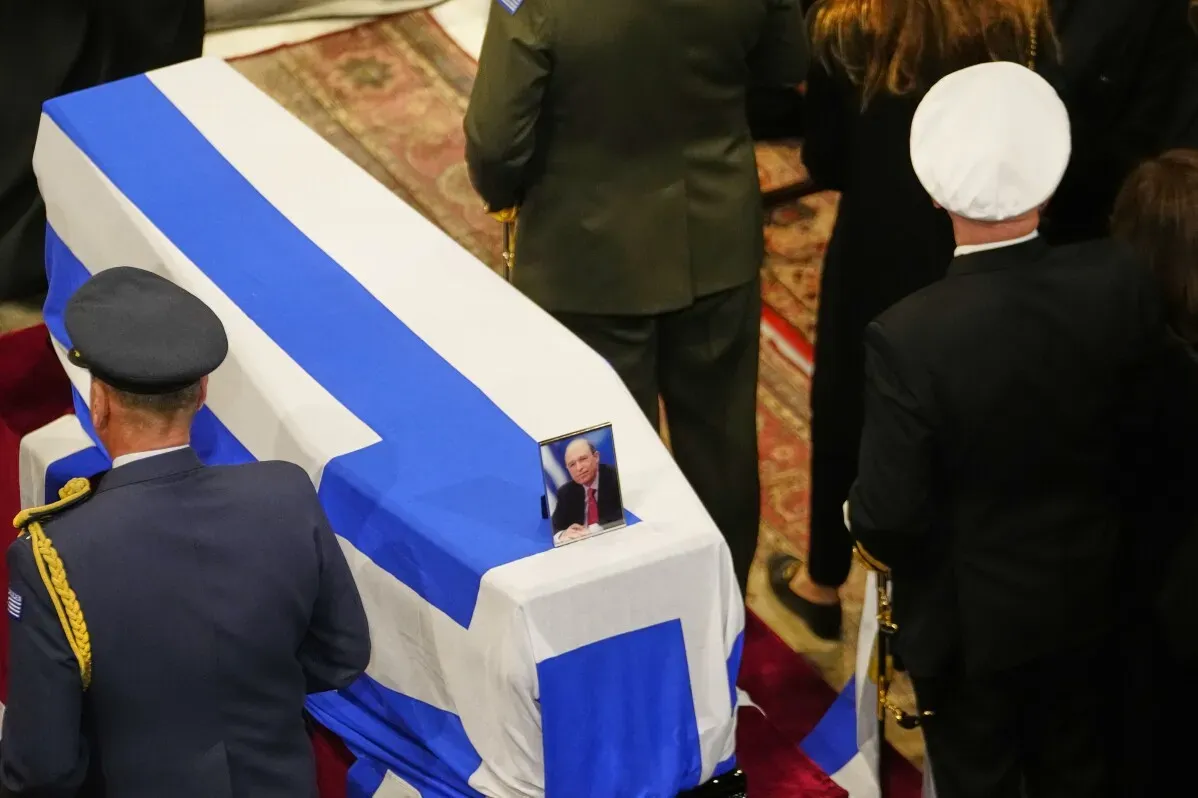 جنازة رئيس الوزراء السابق كوستاس سيميتيش، مع العلم اليوناني يغطي النعش وصورة له، وسط حشد من المشيعين في كاتدرائية أثينا.