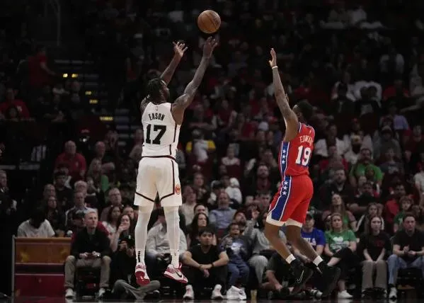 لاعب من هيوستن روكتس يسدد كرة ثلاثية بينما يحاول لاعب من فيلادلفيا 76ers الدفاع عنه، مع جمهور متفاعل في الخلفية.