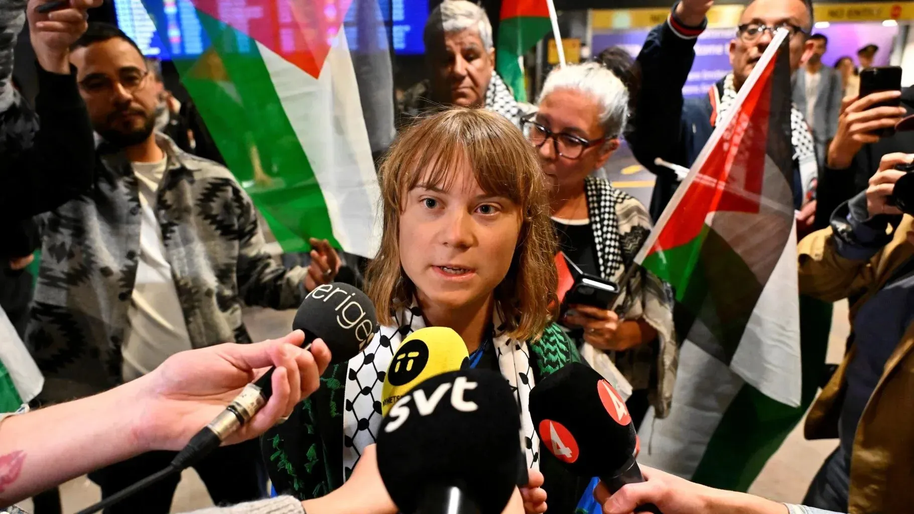 شابة تتحدث إلى وسائل الإعلام وسط حشد يحمل الأعلام الفلسطينية، تعبر عن دعمها للقضية الفلسطينية في ظل الأوضاع الراهنة في غزة.
