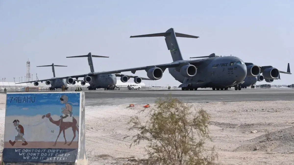 طائرات عسكرية أمريكية من طراز C-17 متوقفة في قاعدة جوية، مع لوحة فنية تُظهر مشهدًا صحراويًا، تعكس التوترات في المنطقة.