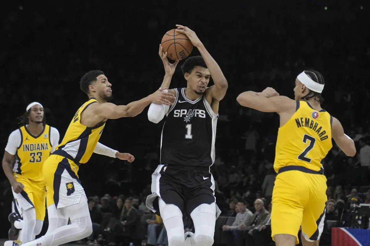 مباراة كرة سلة في دوري الـNBA تُظهر لاعب سان أنطونيو فيكتور ويمبانياما يتلقى ضغطاً من لاعبي إنديانا بيسرز في لحظة حاسمة.