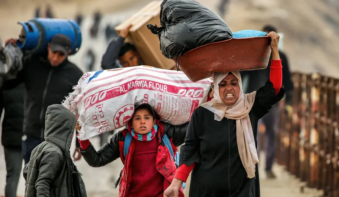نساء وأطفال يحملون أمتعة ثقيلة أثناء عبورهم الحدود المصرية إلى غزة، وسط ظروف إنسانية صعبة ونقص في المساعدات.